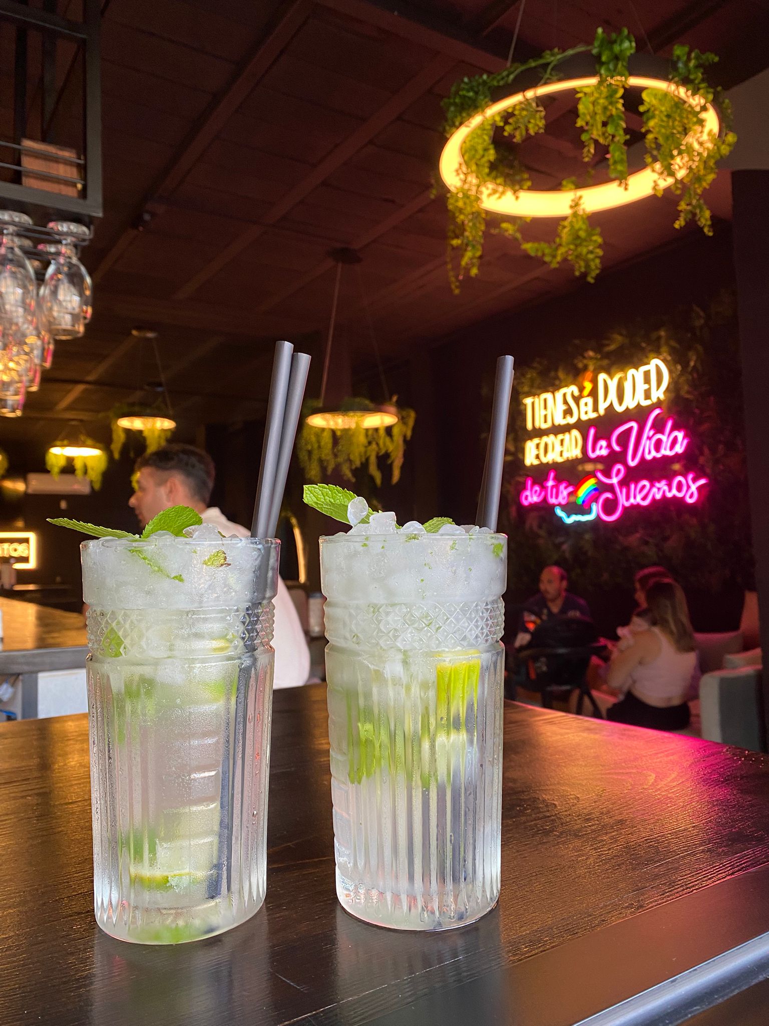 Dos mojitos sobre la barra de madera oscura, con el rótulo de neón rosa del local al fondo