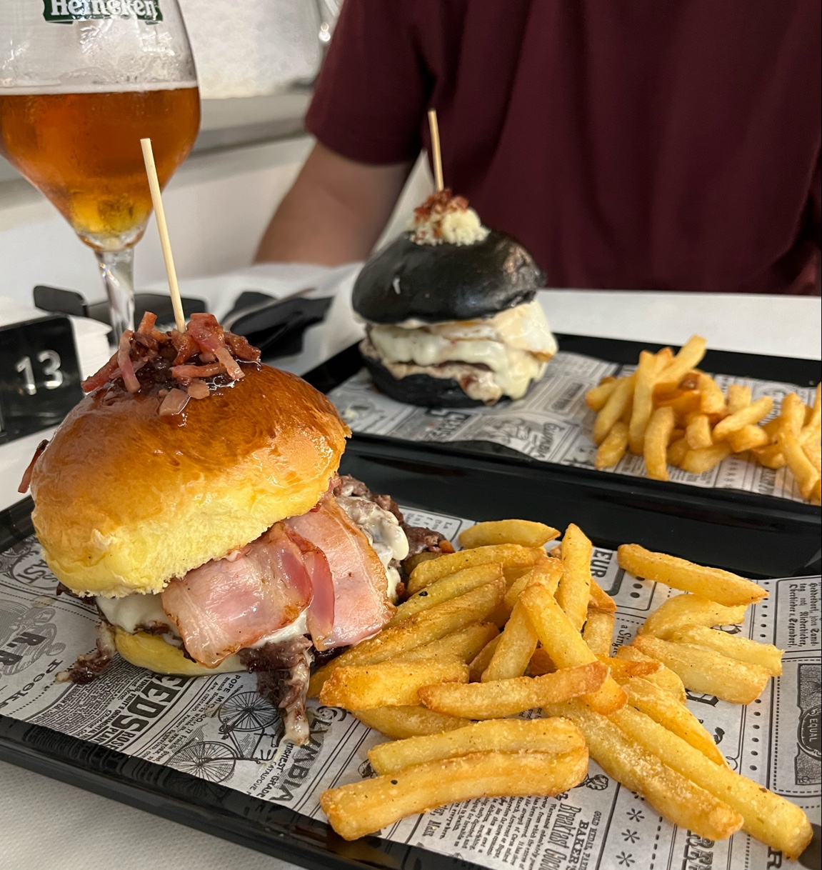Dos hamburguesas, una de pan brioche con bacon y otra de pan negro, con patatas y una cerveza