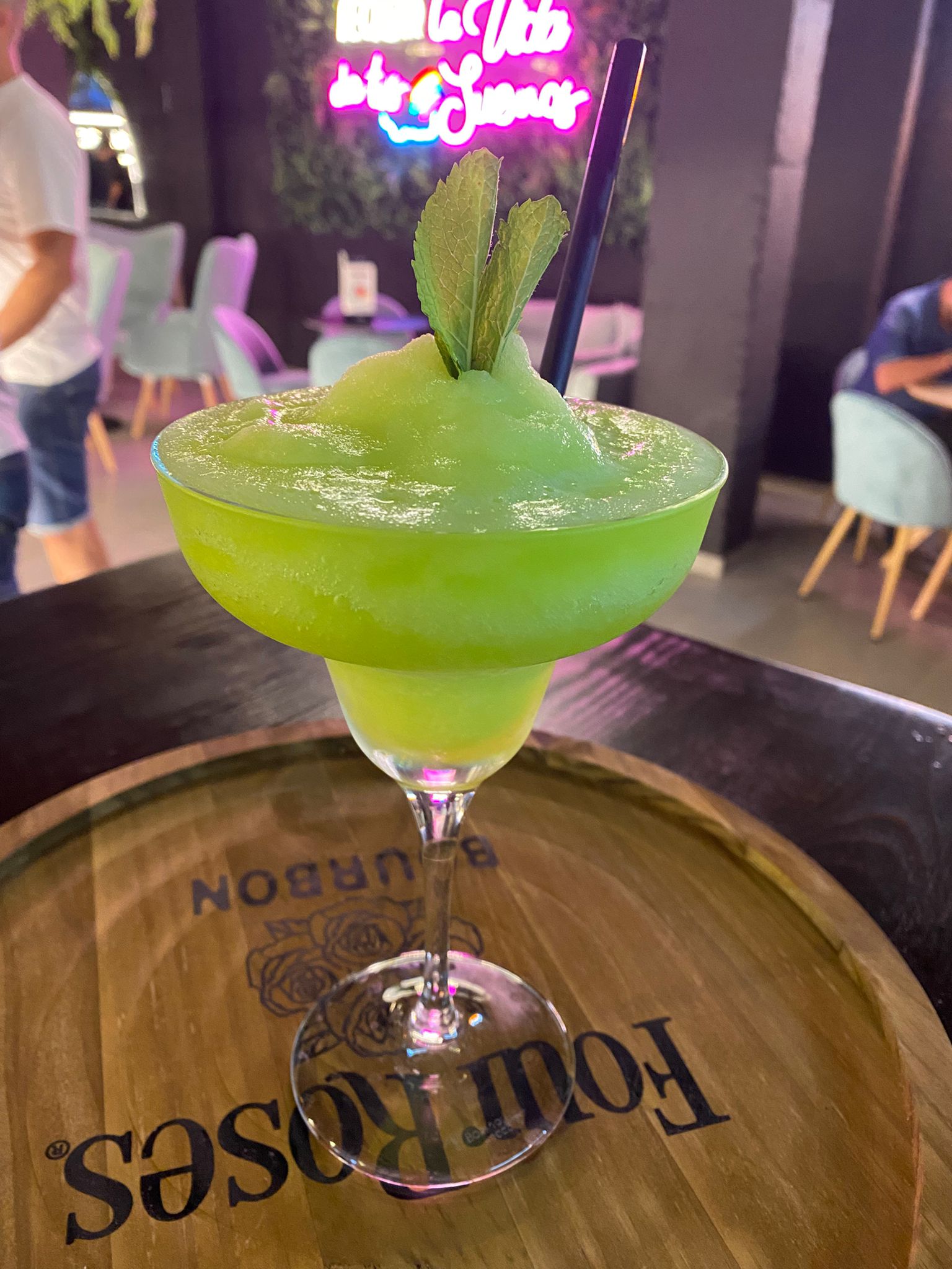 Daiquiri granizado verde con hierbabuena, con el neón rosa del local detrás