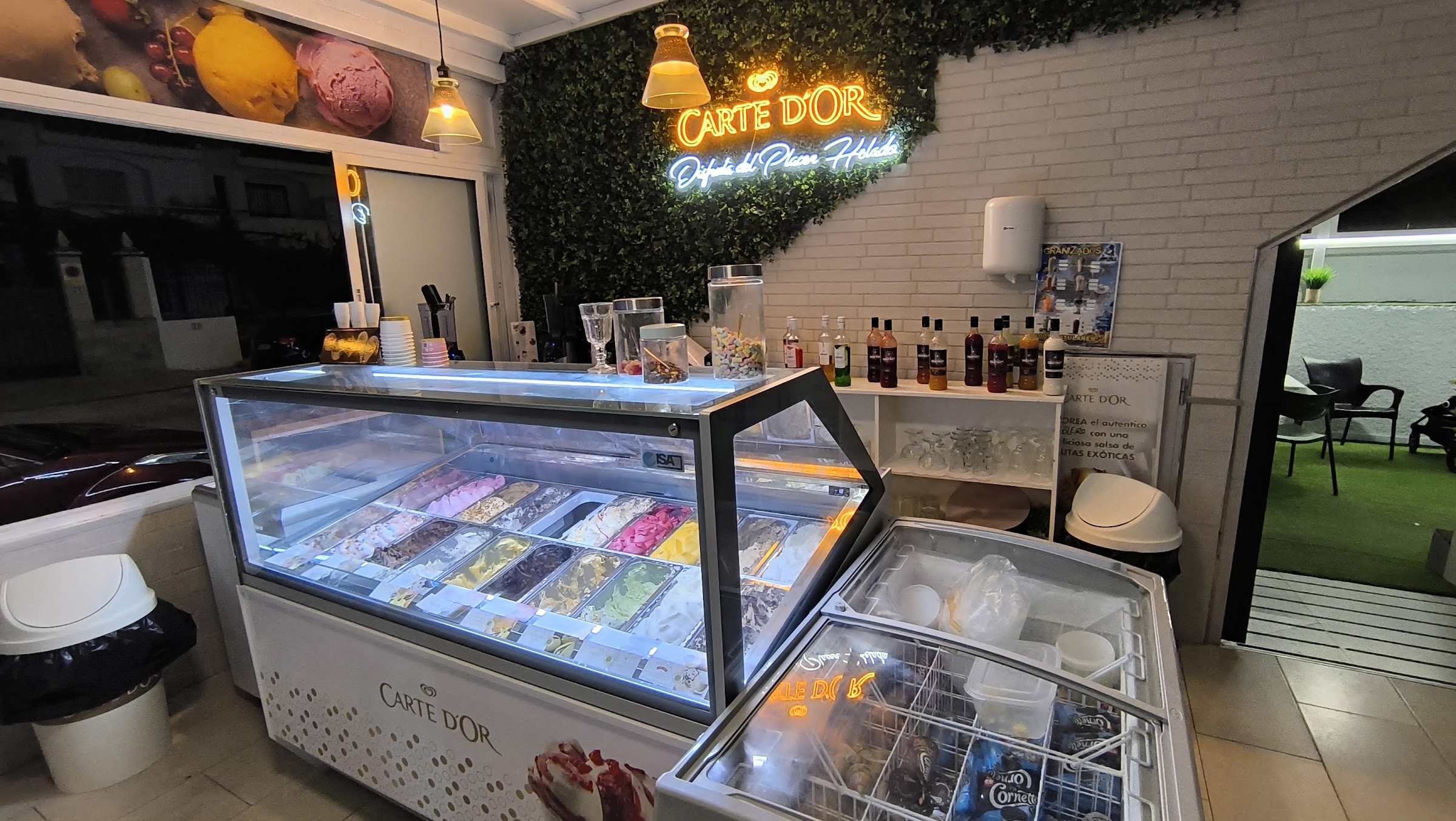 La vitrina de helados de Cuatrocientosmetros encendida de noche, con la pared de hiedra y los rótulos de neón