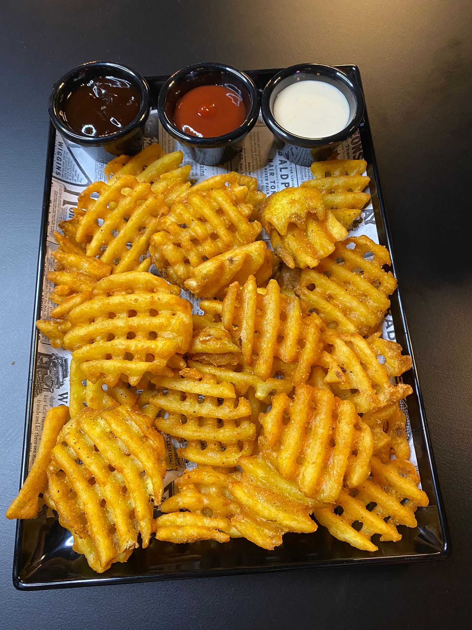 Ración de patatas waffle con salsa barbacoa, kétchup y salsa blanca